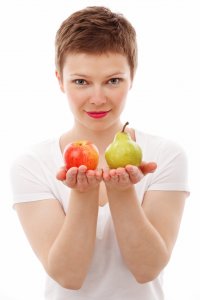 genics-reproducao-humana-assistida-menopausa-3 Mulher na menopausa com camiseta branca e as duas mãos oferecendo futas: maça e pera em cada uma.