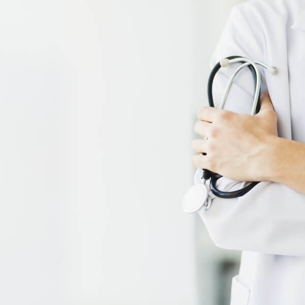 Médico de clínica de reprodução humana com jaleco, de braços cruzados, com estetoscópio em uma das mãos.