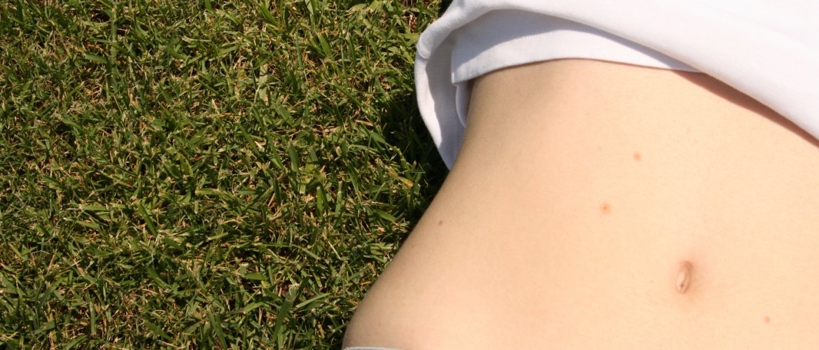 Mulher deitada sobre a grama com blusa levantada e barriga exposta