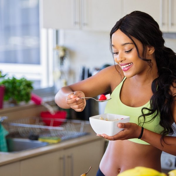 Fertilidade feminina. Mulher se alimentando na cozinha, próxima ao balcão.